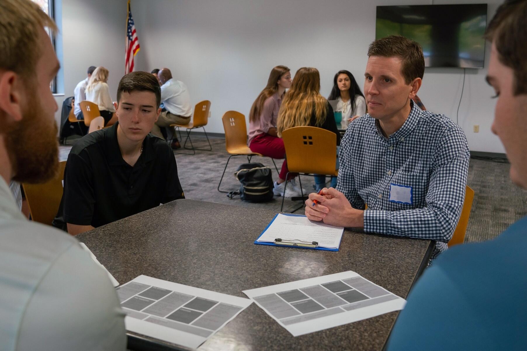 Students present their business idea to community members around a table